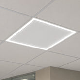 A square LED ceiling light panel glowing brightly within a white acoustic tile ceiling grid.