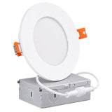 A white circular recessed light fixture with orange release clips, shown mounted on a silver metal junction box with a white connecting cord, isolated on a white background.