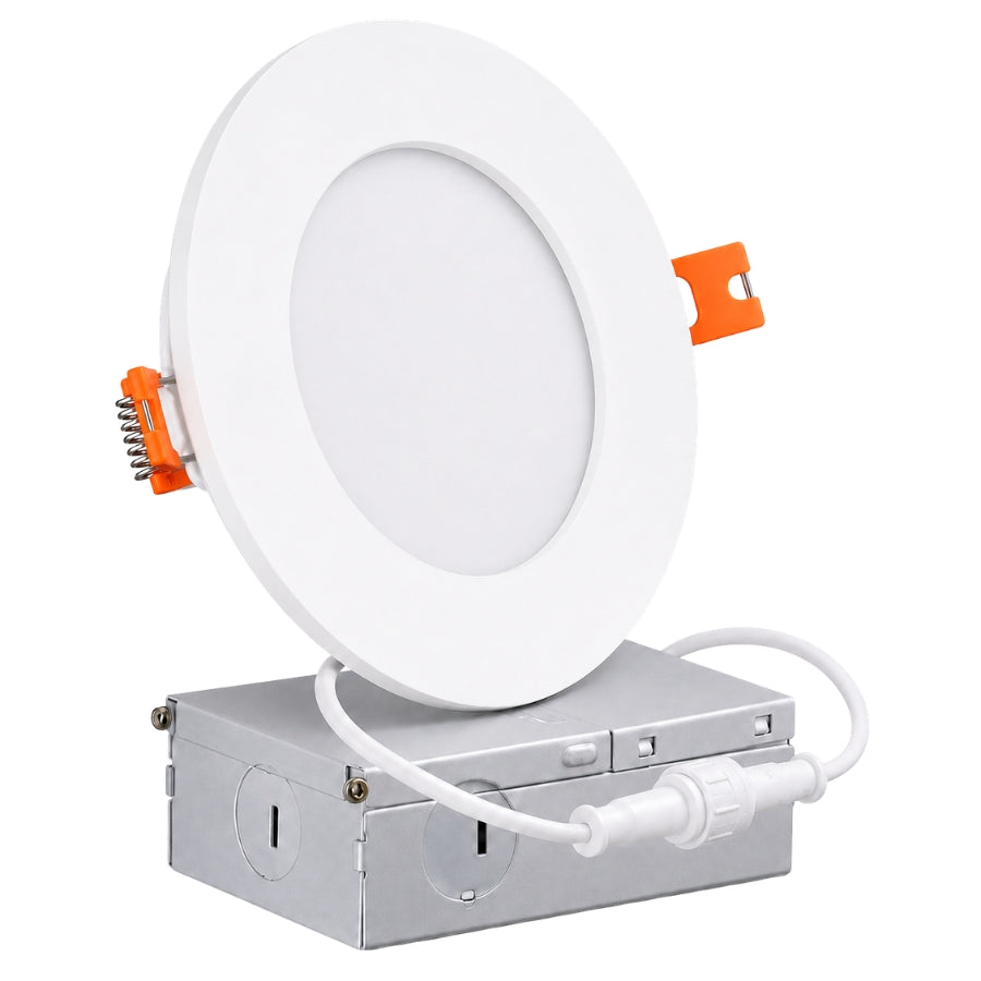 A white circular recessed light fixture with orange release clips, shown mounted on a silver metal junction box with a white connecting cord, isolated on a white background.